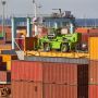 A bright green crane stands on top of stacked shipping containers at a bustling port.