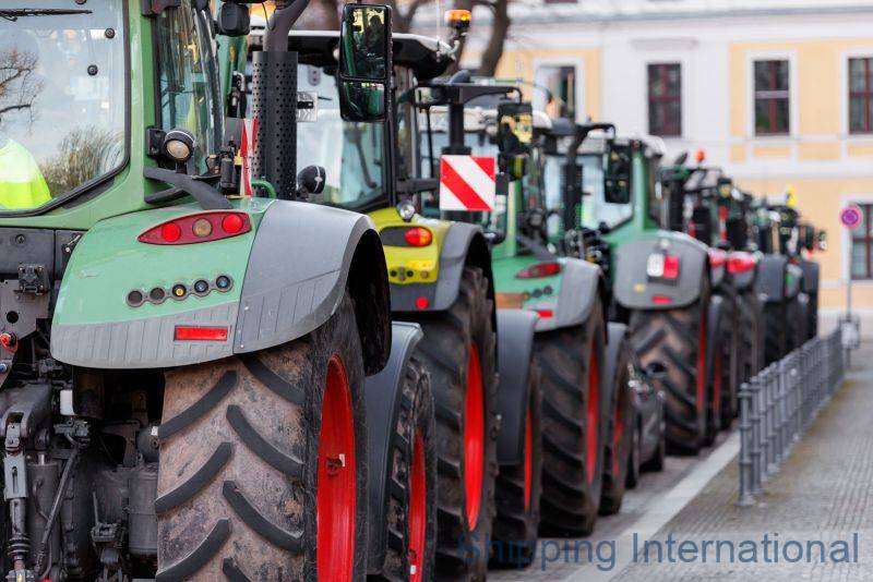 A row of tractors with large tires parked on a street, showcasing their distinctive green and gray designs.